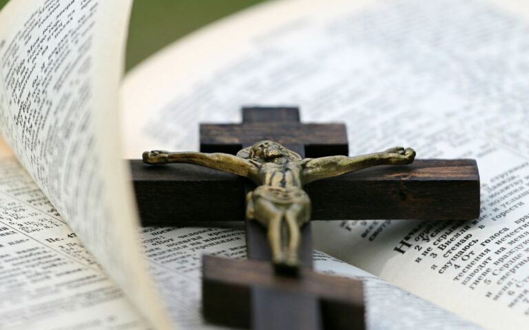 An open Bible with a brass crucifix on a dark wooden cross lying across it.