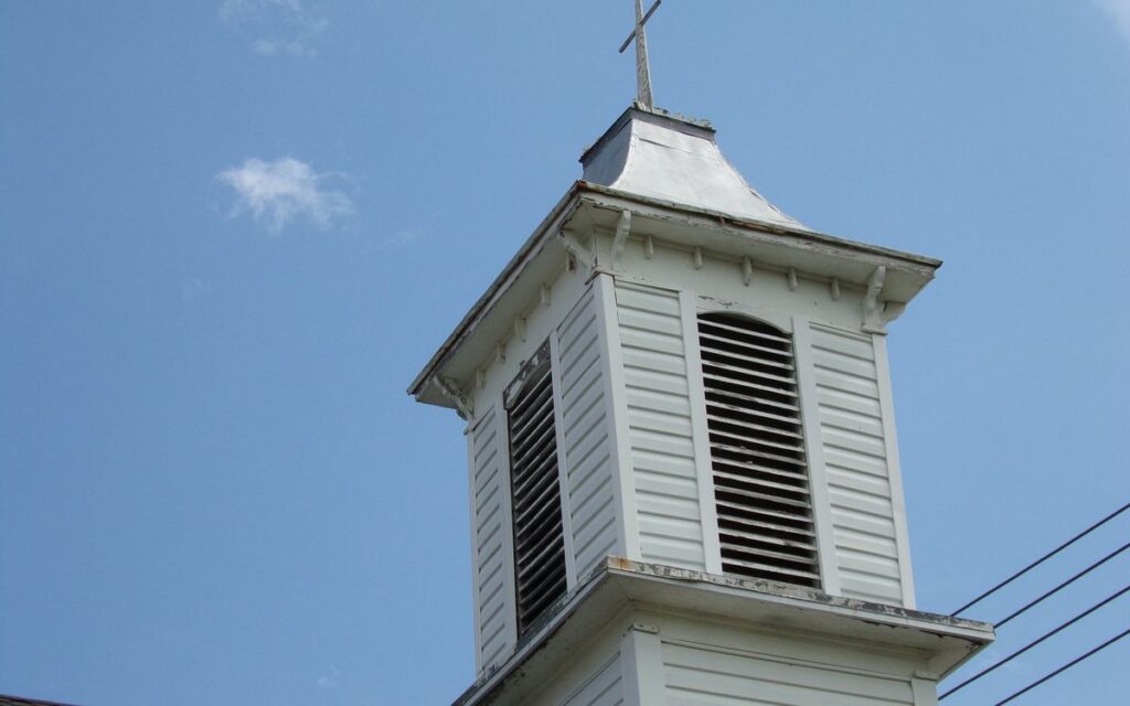 Low angle view of a classic white church steeple with cross, set against a clear sky.