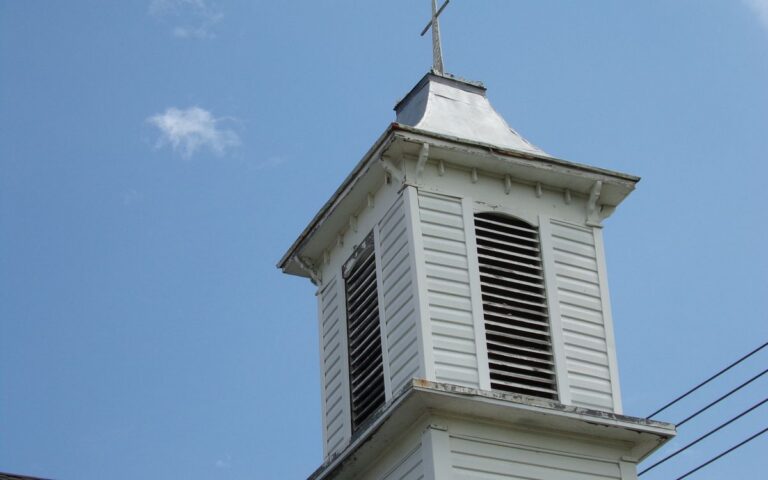 Low angle view of a classic white church steeple with cross, set against a clear sky.