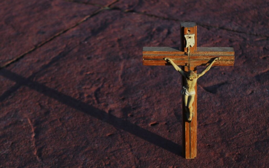 A wooden crucifix casting a shadow on a textured red stone surface.