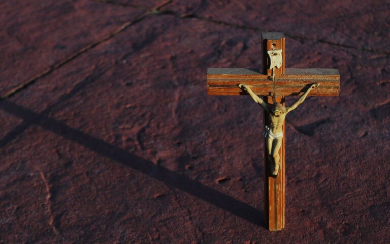 A wooden crucifix casting a shadow on a textured red stone surface.