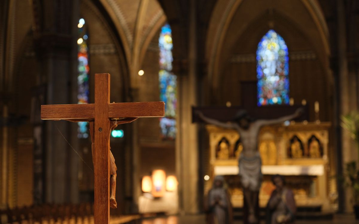 A focused view of a wooden cross in Eindhoven Cathedral with stained glass in the background.