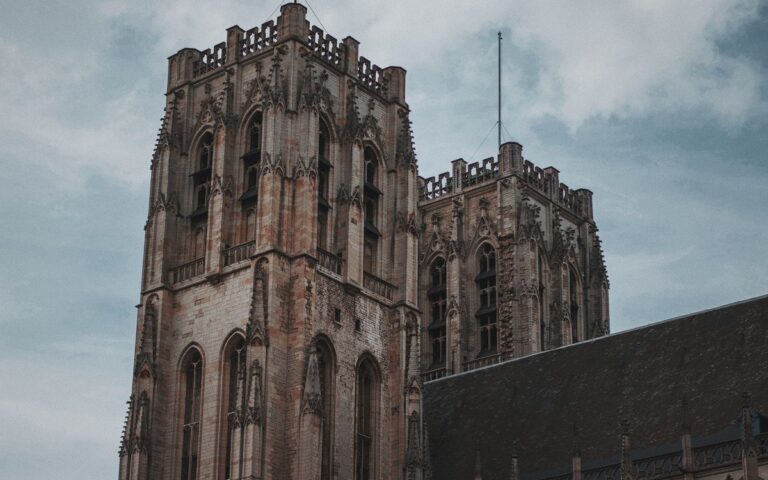 Low angle view of a majestic Gothic cathedral tower showcasing intricate architectural details against a cloudy sky.