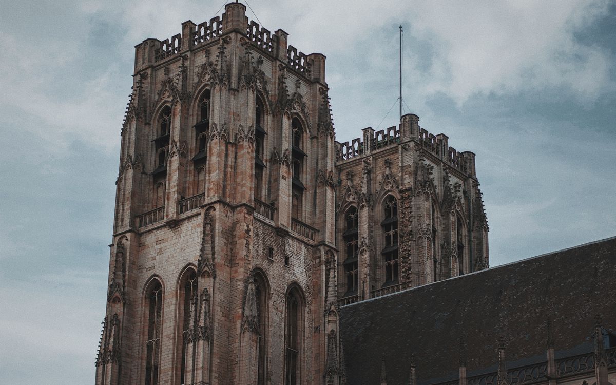 Low angle view of a majestic Gothic cathedral tower showcasing intricate architectural details against a cloudy sky.