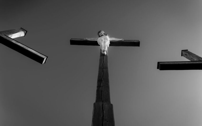 Dramatic black and white photograph depicting three crosses with a central crucifixion scene against a clear sky.