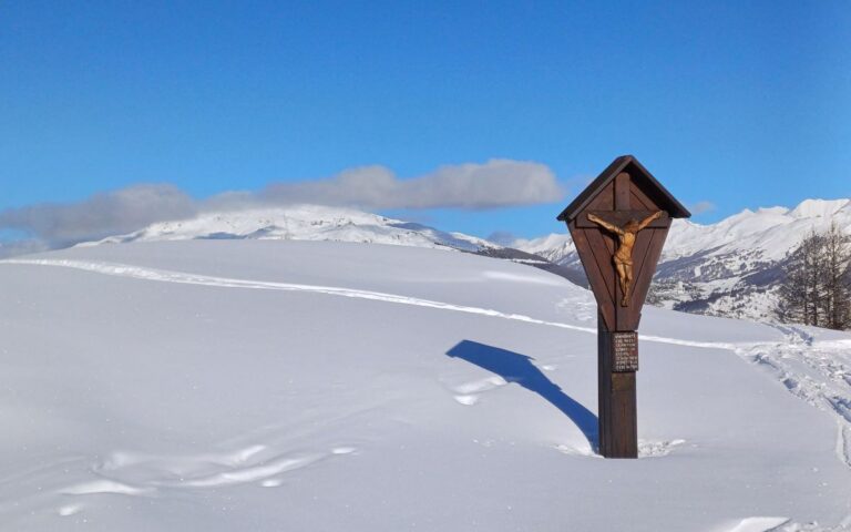 A serene snowy mountain landscape featuring a wooden crucifix under a clear blue sky.