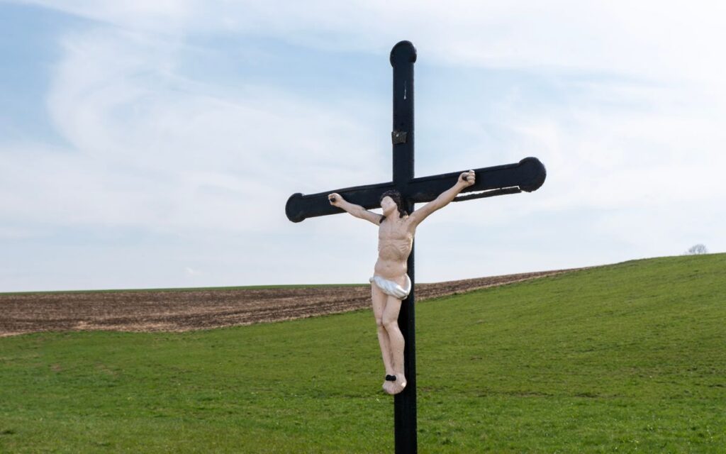 Outdoor crucifixion scene with a cross on a grassy hillside under a clear blue sky.