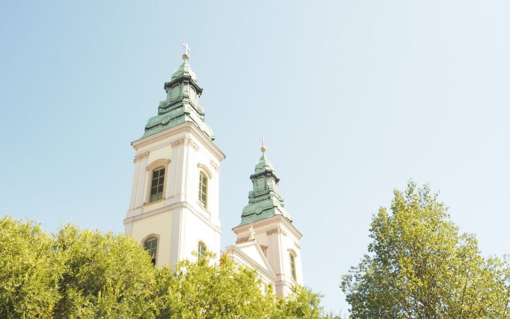 Charming view of historic church towers surrounded by lush greenery under a bright blue sky.