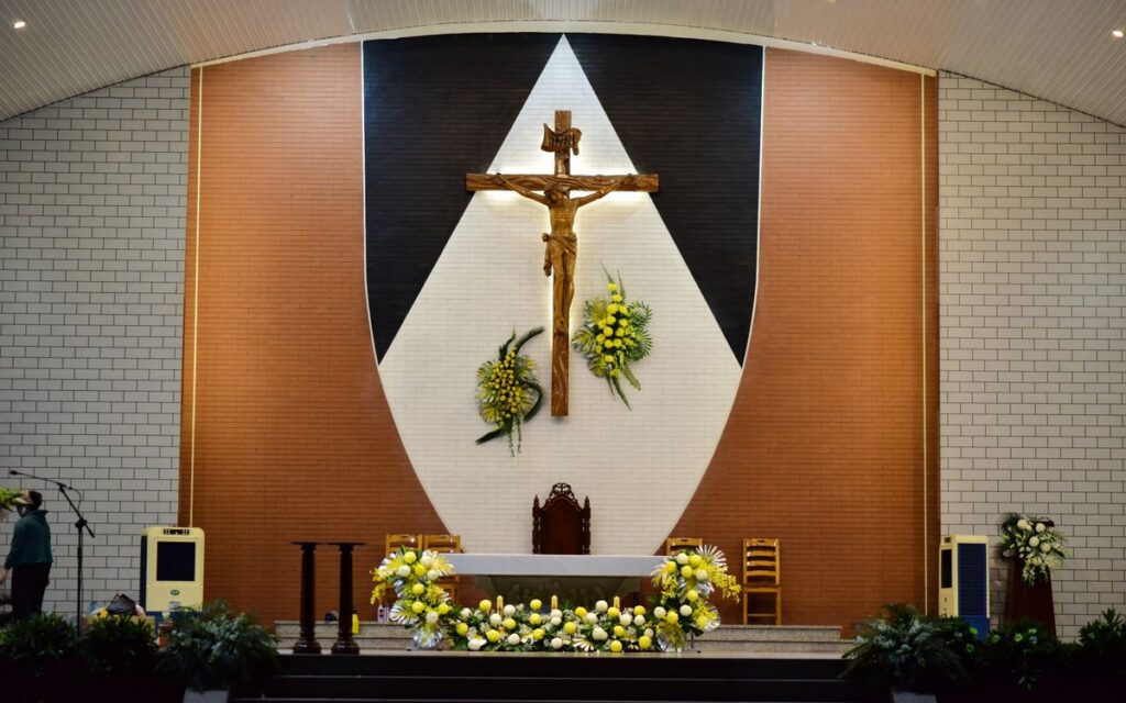 A church altar featuring a prominent crucifix and floral decorations, creating a serene spiritual atmosphere.