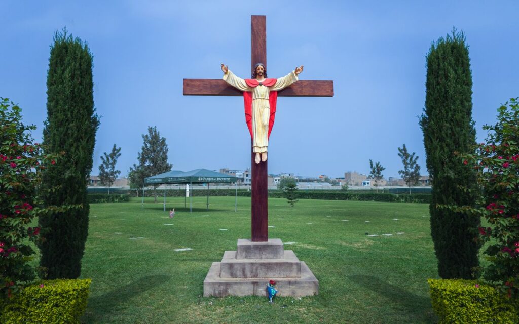 A statue of Jesus on a wooden cross in a landscaped garden with clear skies.