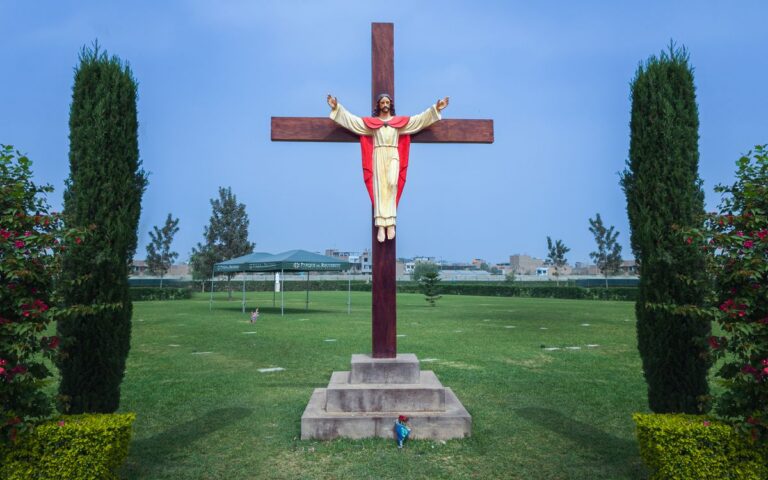 A statue of Jesus on a wooden cross in a landscaped garden with clear skies.
