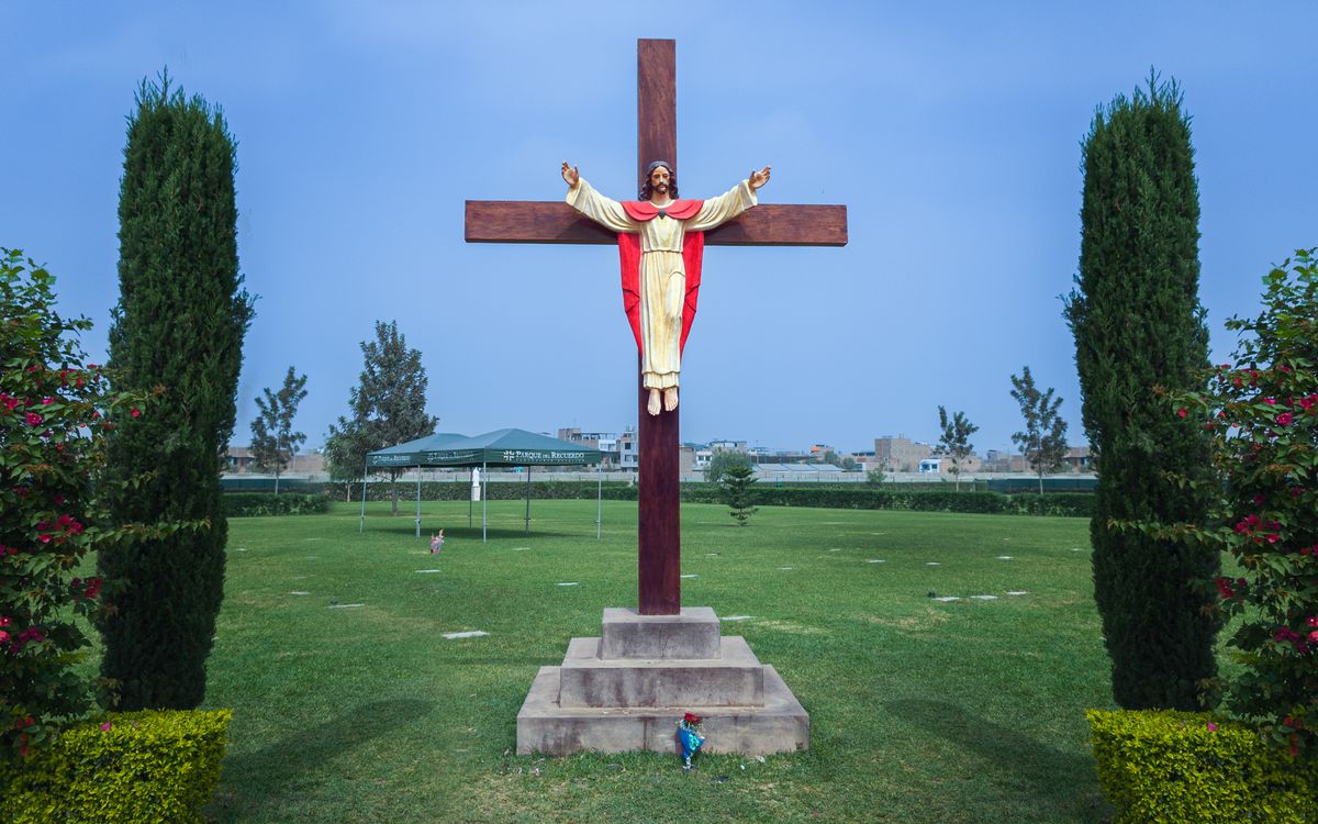 A statue of Jesus on a wooden cross in a landscaped garden with clear skies.