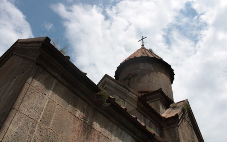 A historic stone church tower with a cross under a partly cloudy sky.