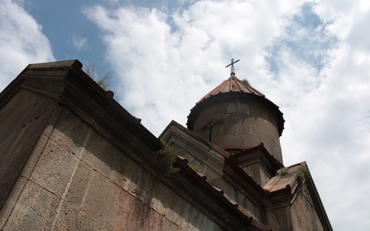 A historic stone church tower with a cross under a partly cloudy sky.