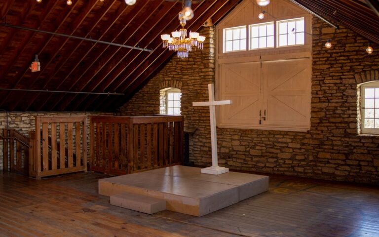 Elegant wooden chapel interior in Rochester, MN, featuring a cross, chandelier, and natural light.