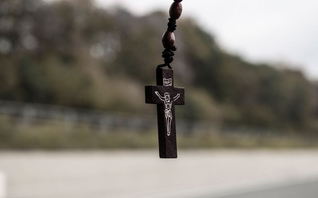 Detailed close-up of a wooden crucifix hanging with a blurred outdoor background.