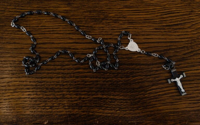 A rosary with black beads and cross on a wooden table.