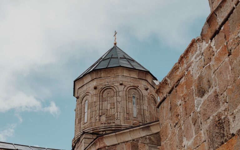 Low angle view of an ancient stone church tower with a cross against a cloudy sky.