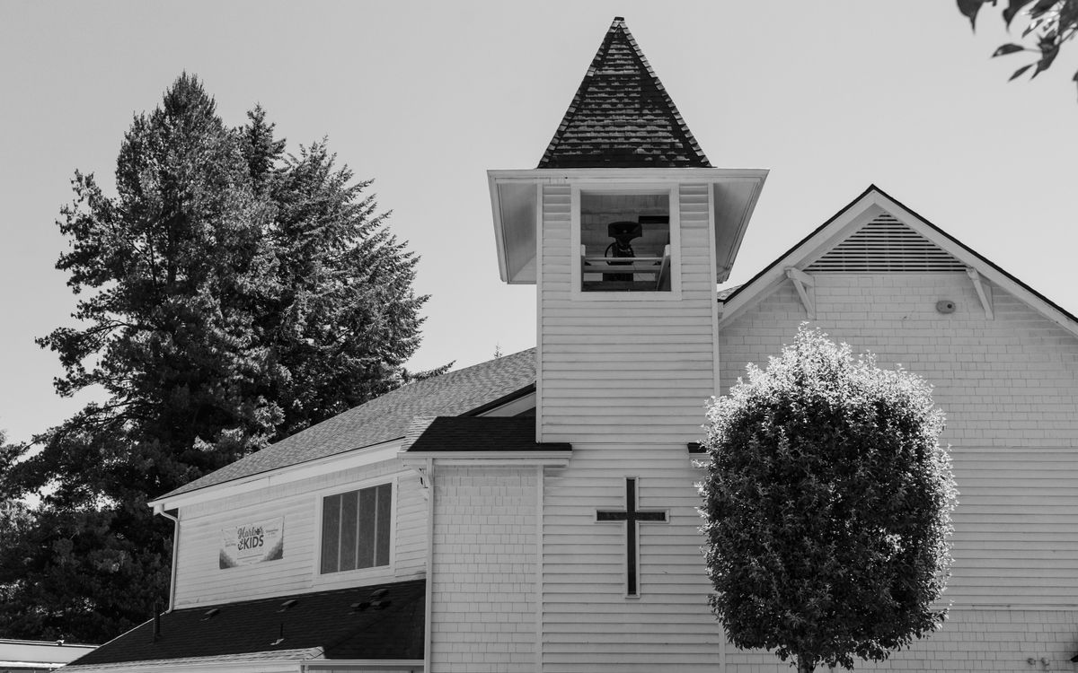 A black and white image of a church with a prominent bell tower and surrounding trees.