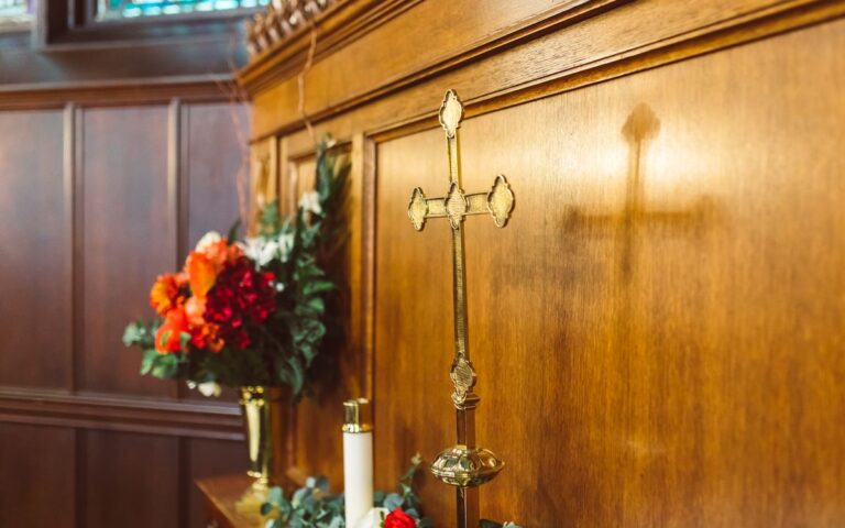 A golden cross on a wooden altar with colorful floral decorations in a church setting.