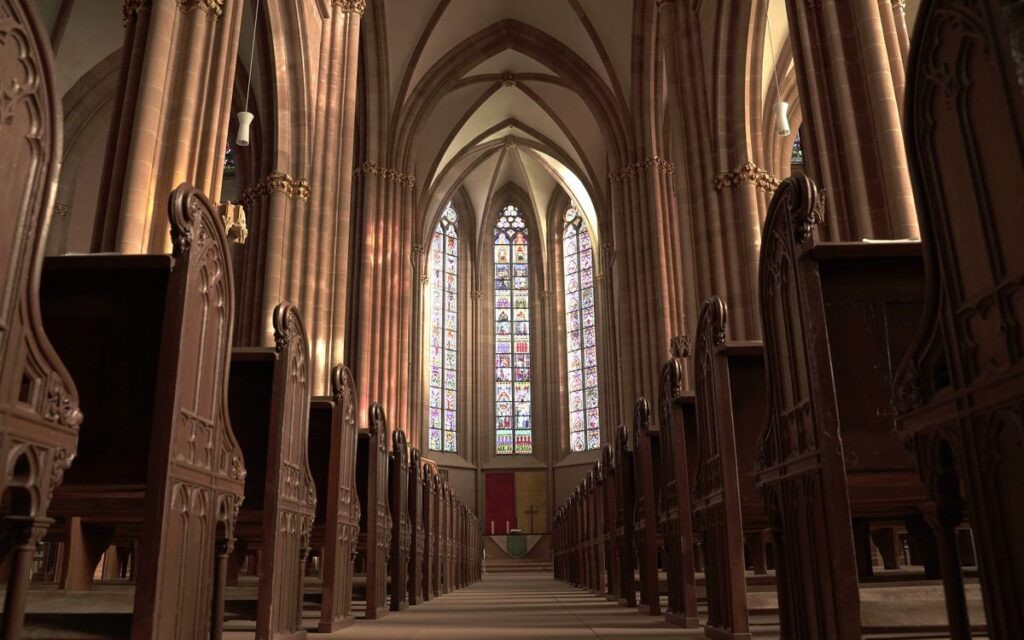 Interior view of a gothic church in Oppenheim, showcasing arches, pews, and stained glass windows.