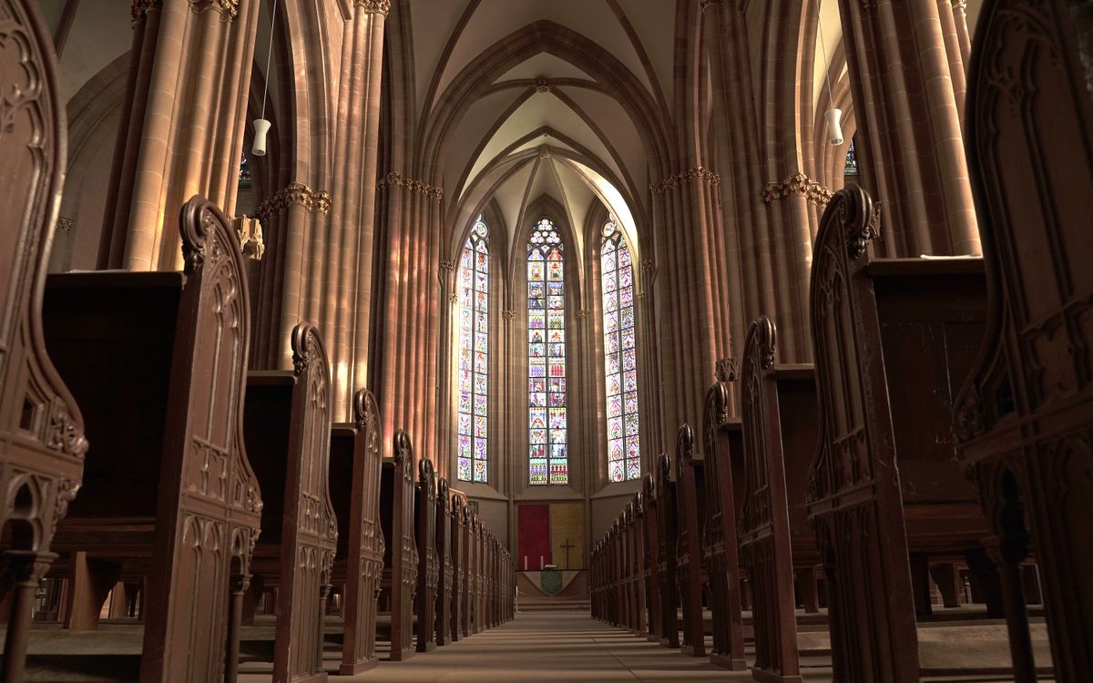 Interior view of a gothic church in Oppenheim, showcasing arches, pews, and stained glass windows.