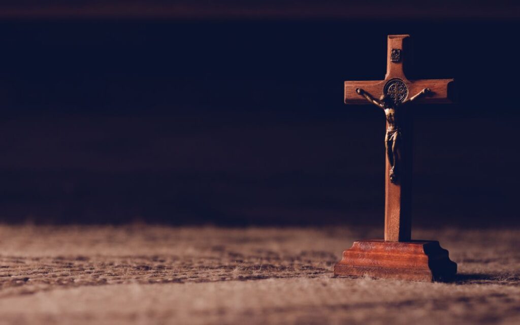 A solitary wooden crucifix stands on a carpet, casting a shadow in dim ambient lighting symbolizing peace and reflection