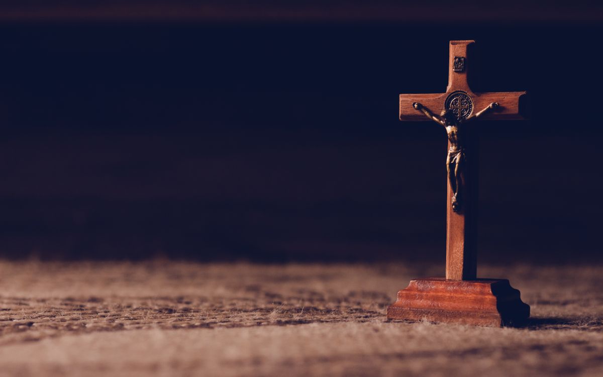 A solitary wooden crucifix stands on a carpet, casting a shadow in dim ambient lighting symbolizing peace and reflection