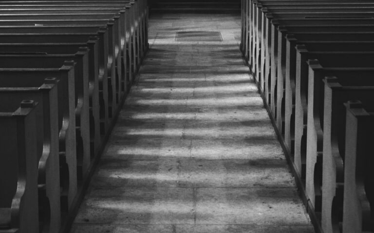 Empty chapel aisle featuring wooden benches under a serene grayscale ambiance.