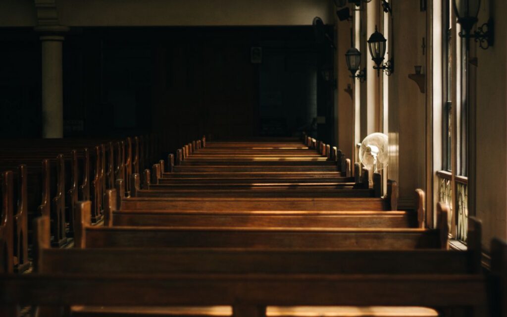 Serene church interior featuring wooden pews and beautiful lighting casting shadows through windows.