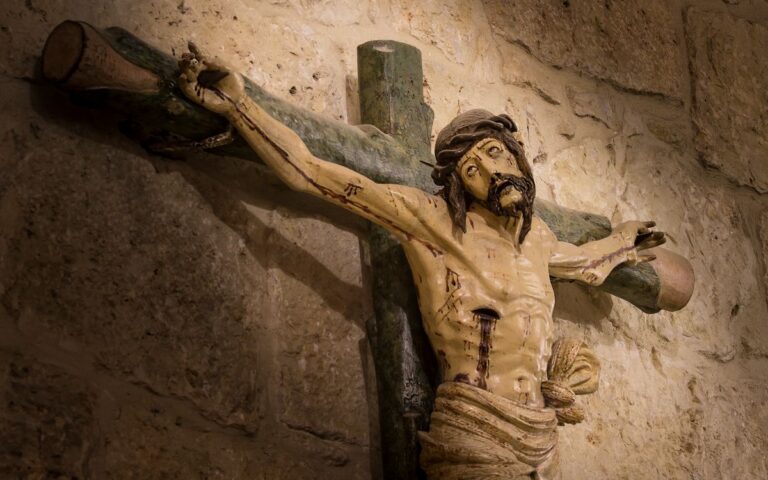 Detailed image of a wooden crucifix sculpture mounted on a stone wall.