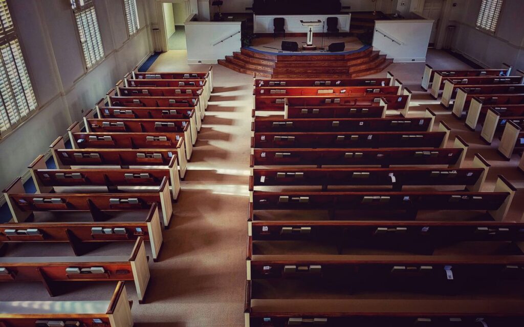 A serene, sunlit view of an empty church with neatly arranged wooden pews and an altar.