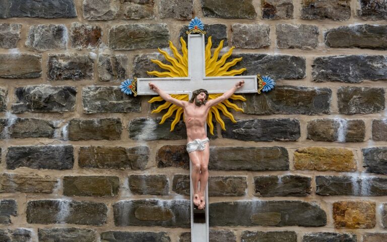 Colorful crucifix with sunburst on an ancient stone wall symbolizing faith.