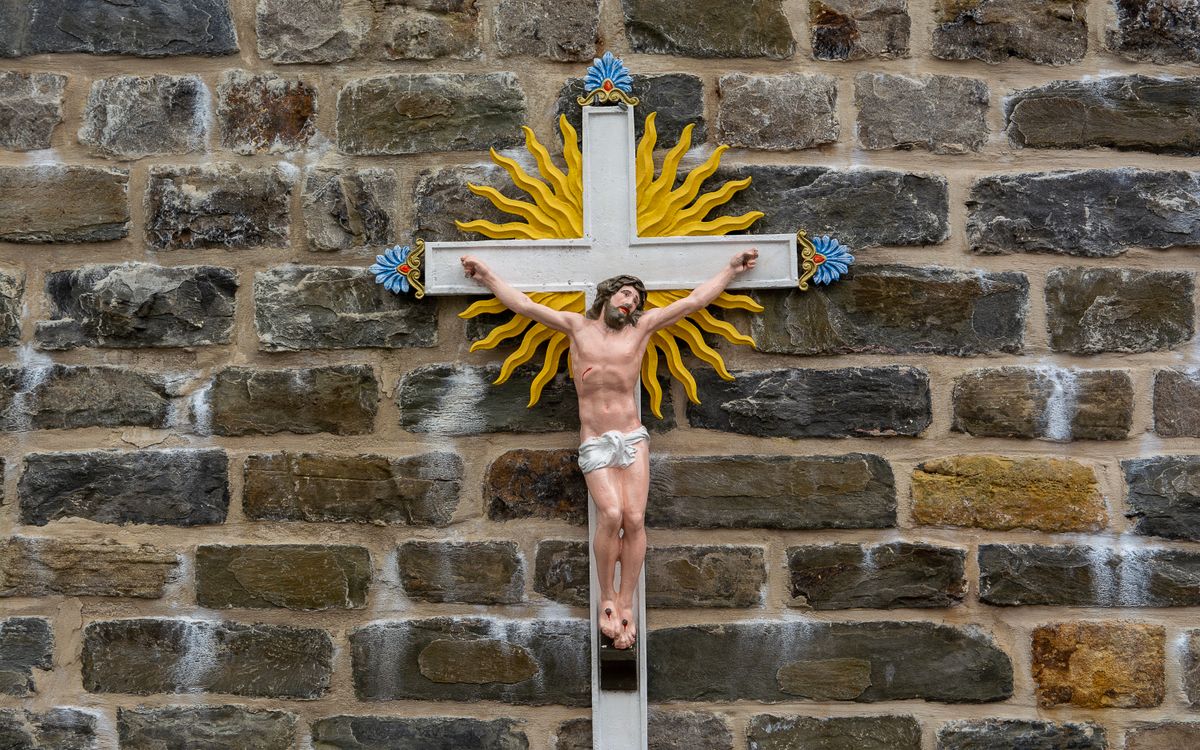 Colorful crucifix with sunburst on an ancient stone wall symbolizing faith.