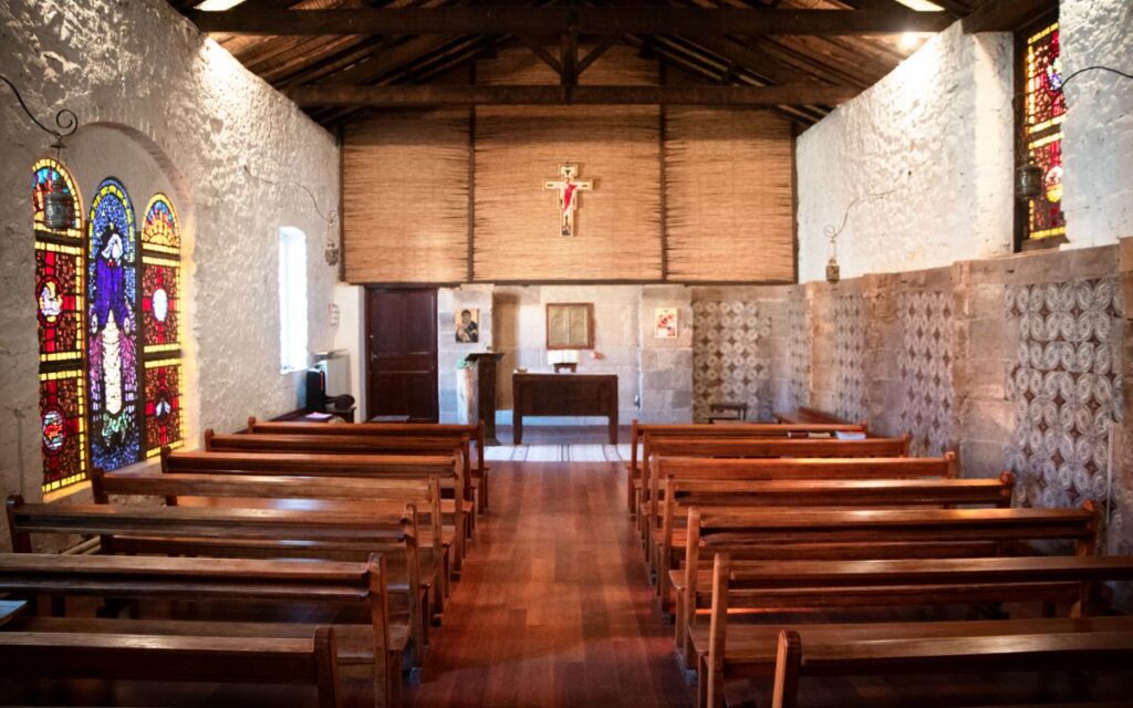 View of the quiet interior of Our Lady of Atlas Monastery in Médéa, featuring wooden pews and stained glass windows.