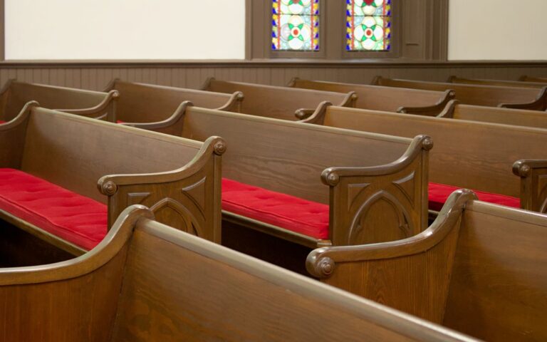 Cozy church interior with wooden pews featuring red cushions, complemented by beautiful stained glass windows.