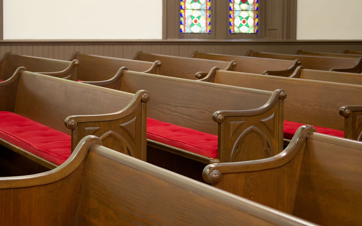 Cozy church interior with wooden pews featuring red cushions, complemented by beautiful stained glass windows.