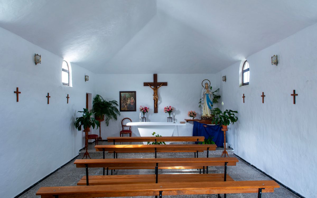 Peaceful interior of a chapel in Guinate, Spain, featuring benches, crosses, and an altar.