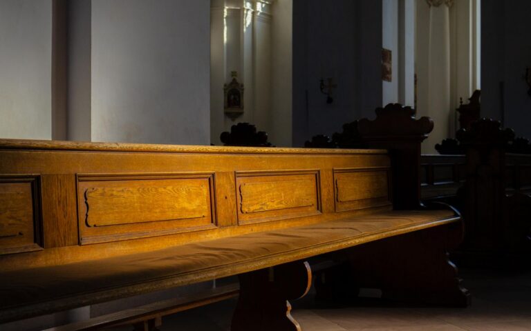 Sunlight highlighting a wooden church pew inside a historic church, creating a serene atmosphere.