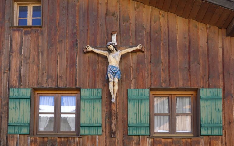 A detailed carved wooden crucifix displayed on the facade of a rustic wooden cabin.
