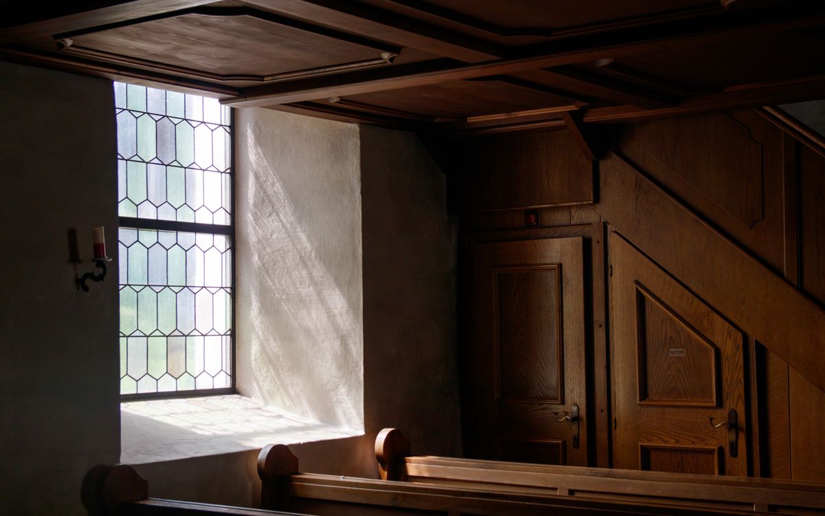 Sunlight streaming through stained glass illuminates a church corner, creating a serene ambiance.