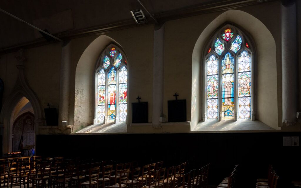 Sunlight illuminates stained glass windows in this serene French church interior.