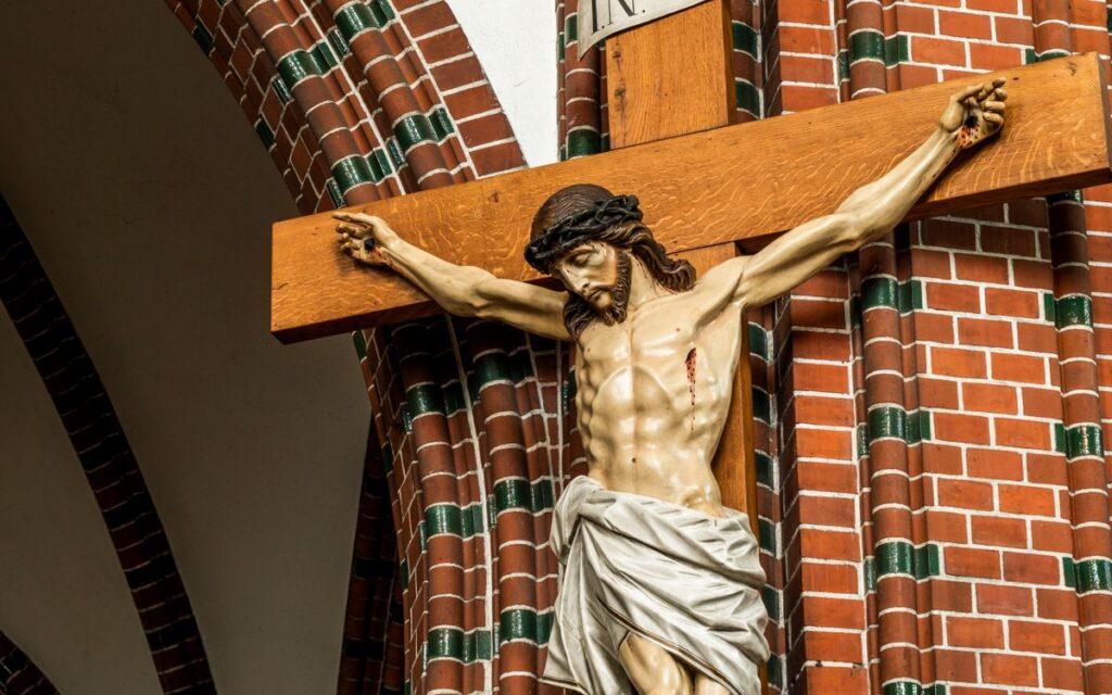 Crucifix sculpture of Jesus on the cross displayed in a brick church interior.