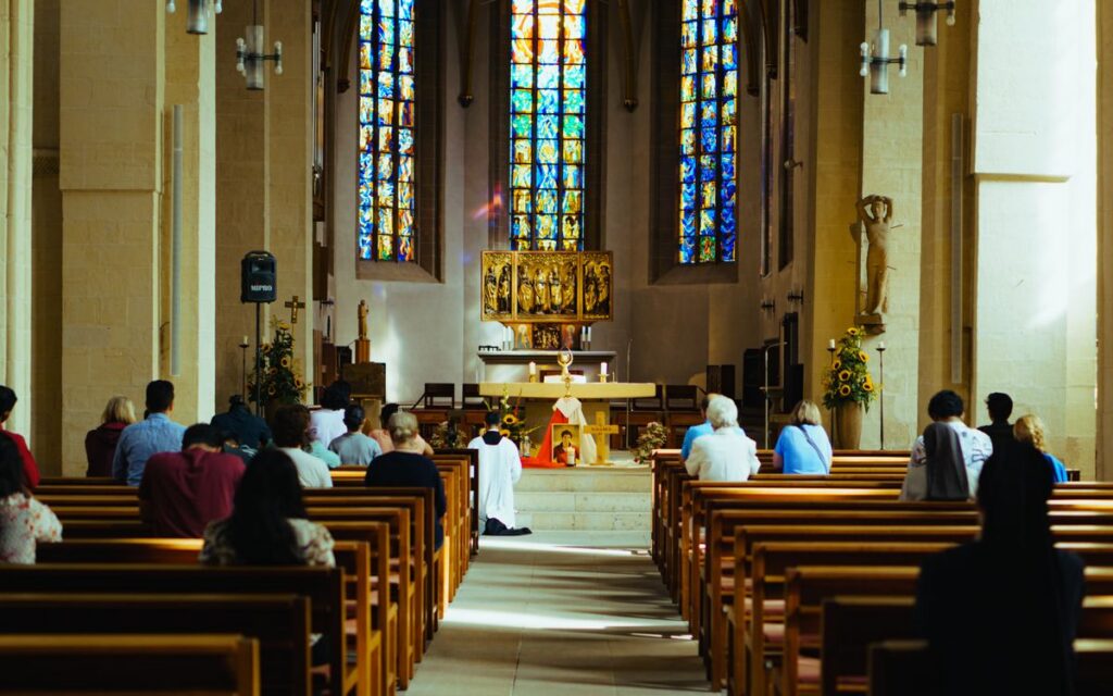 Congregation attending a service in a church with vibrant stained glass windows.
