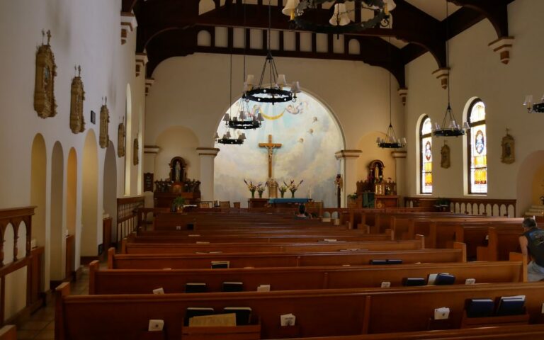 Atmospheric interior of a traditional church with wooden pews and stained glass windows.