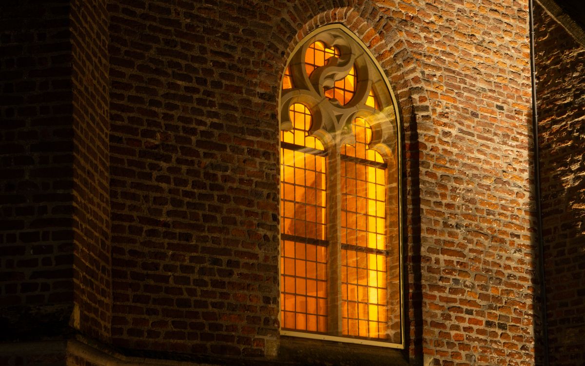 A beautifully illuminated Gothic church window glowing warmly against a brick wall during the night.