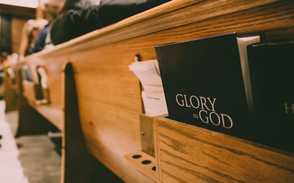 A close-up of a wooden church pew holding hymnals and a Bible, symbolizing worship.