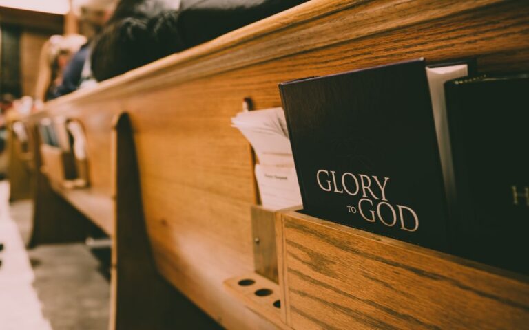 A close-up of a wooden church pew holding hymnals and a Bible, symbolizing worship.