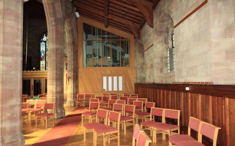 Sunlit seating in a historic church interior with stained glass windows and wooden beams.