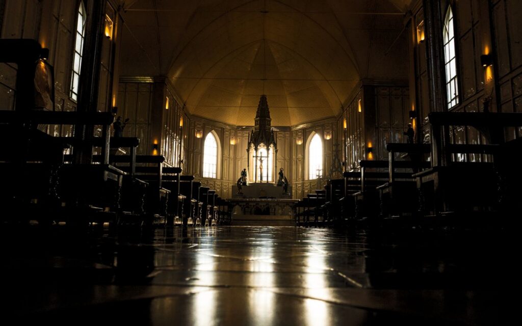Dramatic view of a gothic cathedral interior with rows of benches and altar.